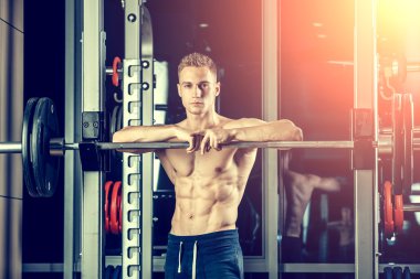 Closeup portrait of a muscular man workout with barbell at gym. Brutal bodybuilder athletic six pack, perfect abs, shoulders, biceps, triceps and chest