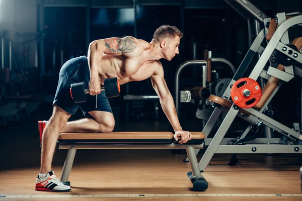 Athlete muscular bodybuilder training back with dumbbell  in the gym — Stock Photo, Image