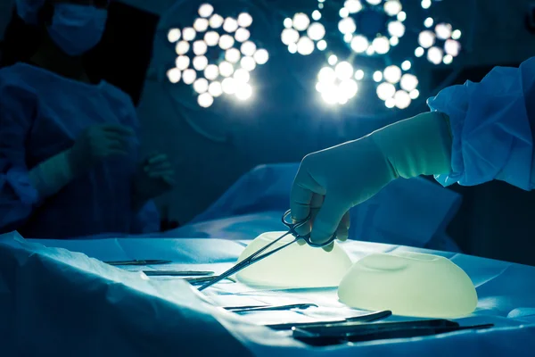 Nurse hand taking surgical instrument for group of surgeons at background operating patient .  breast augmentation — Stock Photo, Image