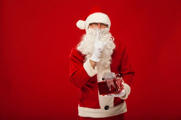 Foto de tipo Santa Claus dando regalo de Navidad y mirando a la cámara. labios secretos de la mano . — Foto de Stock