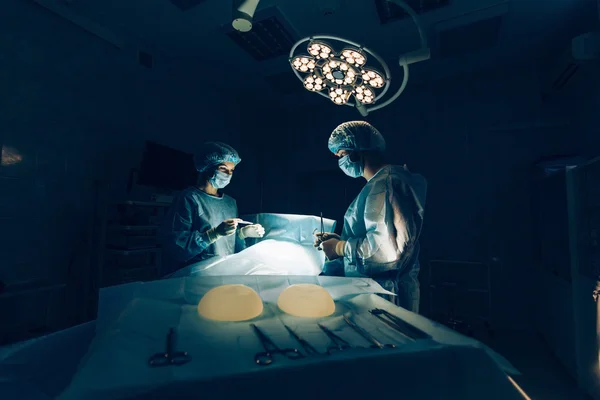 Equipo de cirujanos que trabaja con monitorización de pacientes en quirófano. Aumento de mamas . —  Fotos de Stock