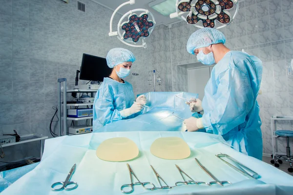 Equipo de cirujanos que trabaja con monitorización de pacientes en quirófano. Aumento de mamas . —  Fotos de Stock