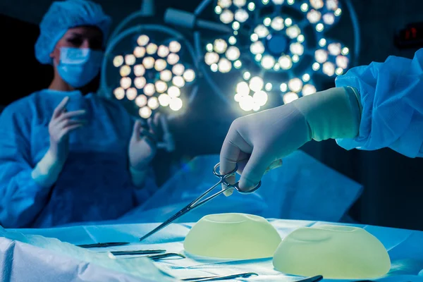 Nurse hand taking surgical instrument for group of surgeons at background operating patient .  breast augmentation — Stock Photo, Image