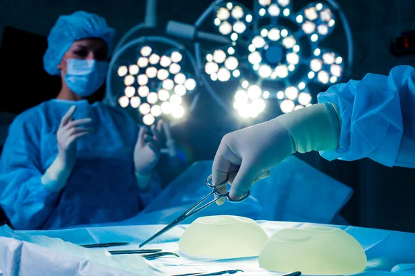 Nurse hand taking surgical instrument for group of surgeons at background operating patient .  breast augmentation — Stock Photo, Image