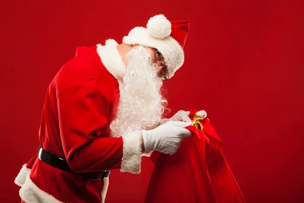 Weihnachtsmann mit großer Tasche auf Schulterbrille roter Hintergrund — Stockfoto