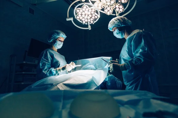 Equipo de cirujanos que trabaja con monitorización de pacientes en quirófano. Aumento de mamas . — Foto de Stock