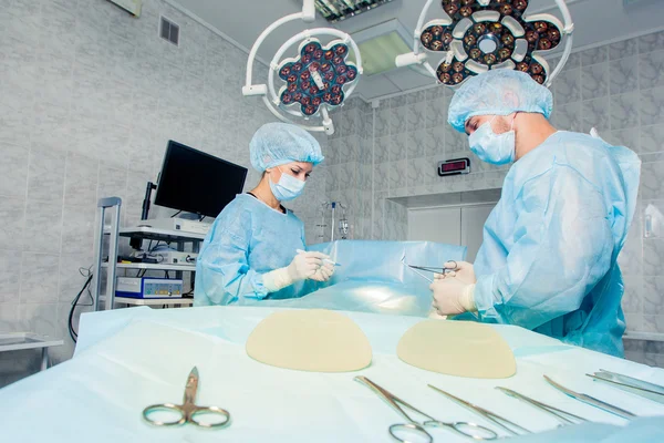 Equipo de cirujanos que trabaja con monitorización de pacientes en quirófano. Aumento de mamas . —  Fotos de Stock