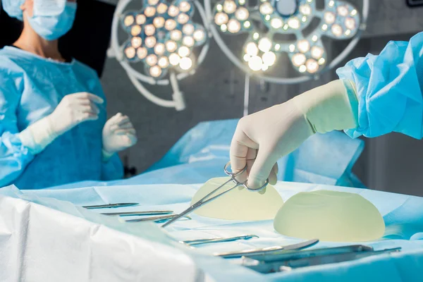 Sjuksköterska hand med kirurgiska instrument för grupp kirurger på bakgrunden operativa patienten. Bröstförstoring — Stockfoto