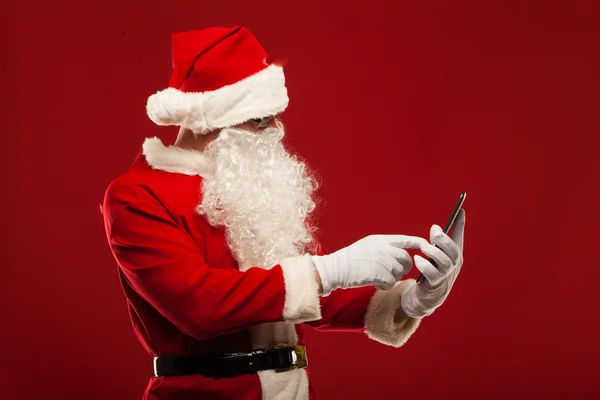 Moderní santa claus pomocí počítače tablet pc na červeném pozadí. Vánoční — ストック写真