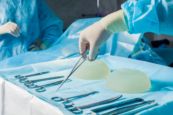 Krankenschwester Hand nimmt chirurgisches Instrument für Gruppe von Chirurgen am Hintergrund operierenden Patienten. Brustvergrößerung — Stockfoto