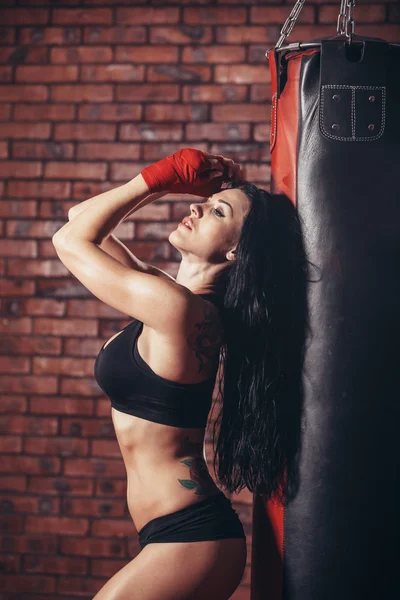 Jovem bela mulher boxer sexy com bandagem de boxe vermelho nas mãos. saco de pancada. a parede de fundo de tijolo . — Fotografia de Stock