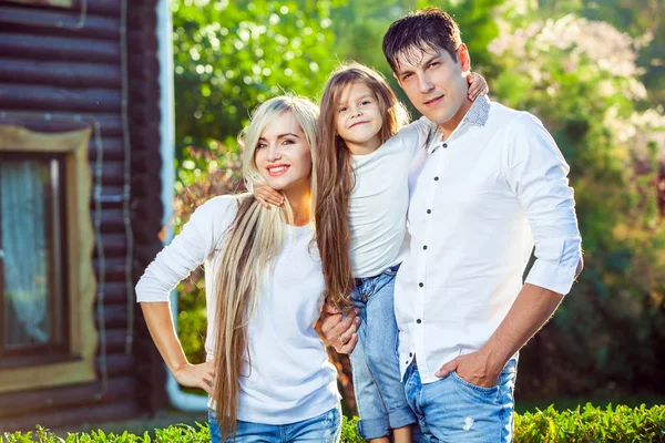 Familia feliz con niño al aire libre, sobre el fondo de una casa de madera en jeans —  Fotos de Stock