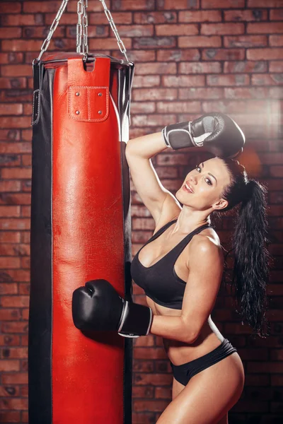 Joven chica sexy con guantes de boxeo, saco de boxeo, en la pared de fondo de ladrillo rojo . —  Fotos de Stock