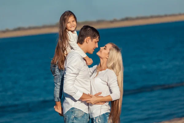 Ung familj i blå jeans kramas på bakgrund av vatten — Stockfoto