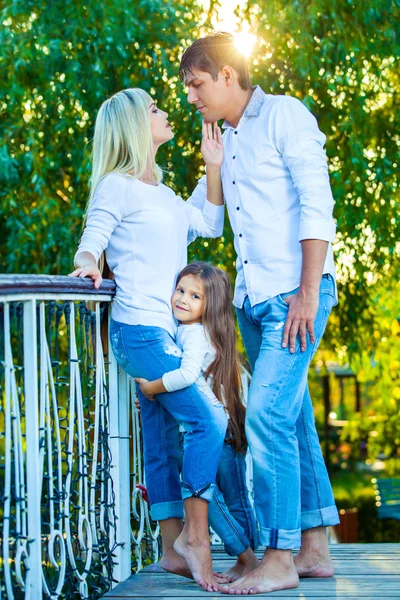 Mamá, papá y el niño se ríen abrazándose, disfrutando de la naturaleza afuera. en jeans azules camisas blancas —  Fotos de Stock