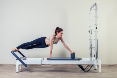 Pilates reformer workout exercises woman brunette at gym indoor clipart