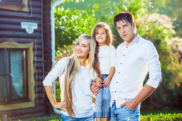 Familia feliz con niño al aire libre, sobre el fondo de una casa de madera en jeans —  Fotos de Stock