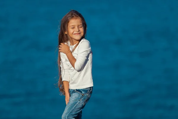 Manis tersenyum gadis kecil di pantai liburan. jeans . — Stok Foto