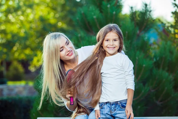 Kobieta szczotkowanie jej córka włosy na zewnątrz dżinsy — Zdjęcie stockowe