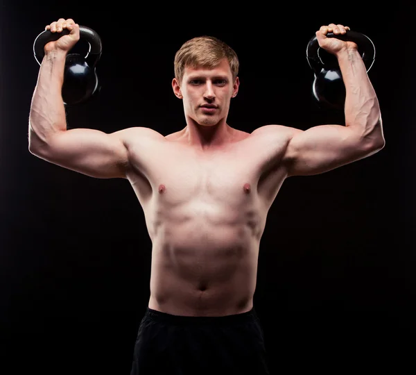 Przystojny facet mięśni Kettlebells na białym tle na czarnym tle — Zdjęcie stockowe
