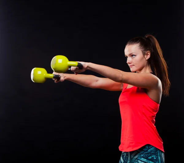 Mujer joven fitness en camisa roja de pie con kettlebells sobre fondo negro —  Fotos de Stock