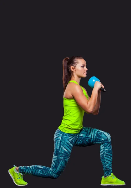 Young woman smiling while using kettlebells against a gray background — Stock Photo, Image