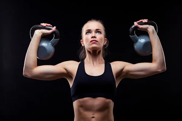 Fitness jonge vrouw met kettlebells op zwarte achtergrond Rechtenvrije Stockfoto's