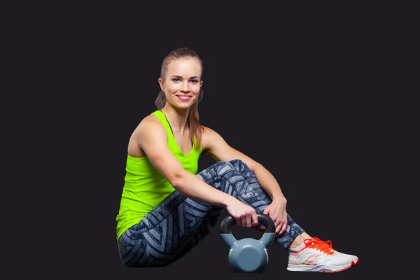 Mujer joven sonriendo mientras usa kettlebells sobre un fondo gris — Foto de Stock