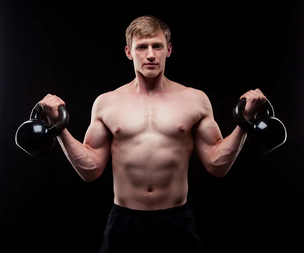 Handsome muscular guy with kettlebells isolated on black background — Stock Photo, Image