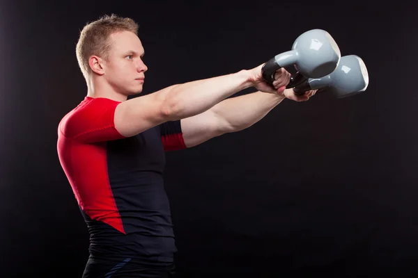 一个人站立与 kettlebellss 在黑色背景上的肖像 — 图库照片