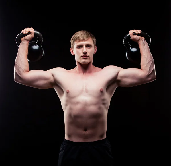 Przystojny facet mięśni Kettlebells na białym tle na czarnym tle — Zdjęcie stockowe
