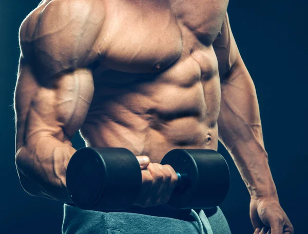 Closeup of a muscular young man lifting dumbbells weights on dark background — Stock Photo, Image