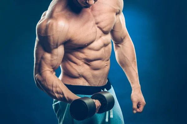 Closeup of a muscular young man lifting dumbbells weights on dark background — Stock Photo, Image