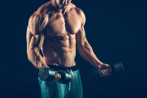 Closeup of a muscular young man lifting dumbbells weights on dark background — Stock Photo, Image