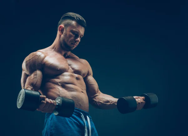 Primer plano de un joven musculoso levantando pesas de pesas sobre fondo oscuro —  Fotos de Stock