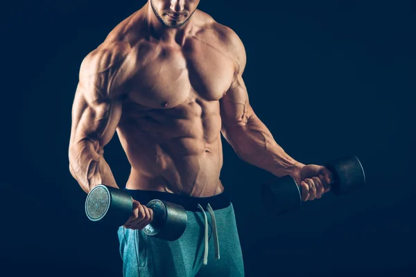 Primer plano de un joven musculoso levantando pesas de pesas sobre fondo oscuro — Foto de Stock