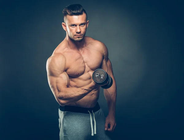 Primer plano de un joven musculoso levantando pesas de pesas sobre fondo oscuro — Foto de Stock