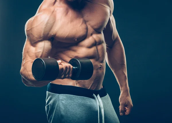 Primer plano de un joven musculoso levantando pesas de pesas sobre fondo oscuro — Foto de Stock