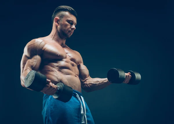 Primer plano de un joven musculoso levantando pesas de pesas sobre fondo oscuro —  Fotos de Stock