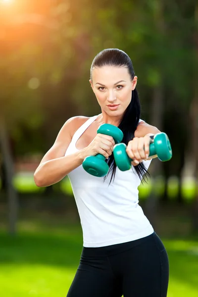 Retrato de mujer alegre en ropa de fitness haciendo ejercicio con mancuerna, al aire libre —  Fotos de Stock