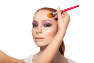 Profesyonel makyöz seksi kırmızı saç modeli makyaj yapıyor. İzole arka plan.