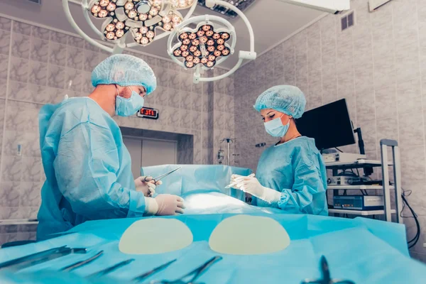 Kirurger team som arbetar med övervakning av patient i kirurgisk operationssalen. Bröstförstoring — Stockfoto