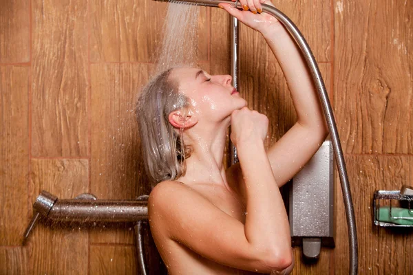 Hermosa mujer parada en la ducha. Ella sostiene en su cabeza de ducha de la mano — Foto de Stock