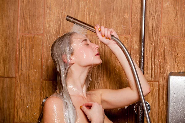 Hermosa mujer parada en la ducha. Ella sostiene en su cabeza de ducha de la mano — Foto de Stock
