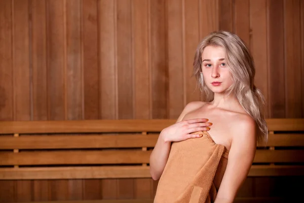 Hermosa mujer sentada relajada en una sauna de madera toalla marrón — Foto de Stock