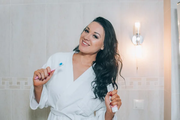 Porträt einer attraktiven Frau beim Zähneputzen im Badezimmer mit weißem Mantel. gesunde Zähne. — Stockfoto