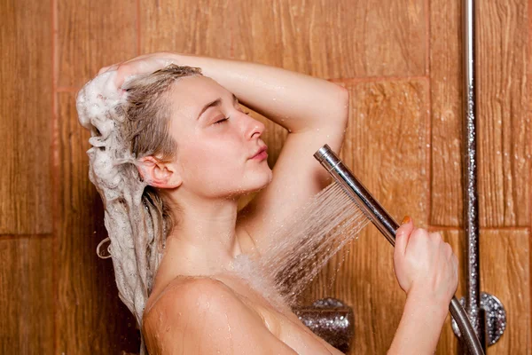 Schöne Frau steht unter der Dusche. hält sie einen Brausekopf in der Hand — Stockfoto