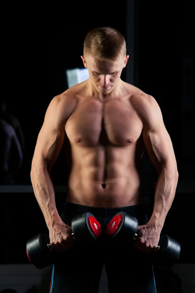 Handsome power athletic man with dumbbell confidently looking forward. Strong bodybuilder six pack, perfect abs, shoulders, biceps, triceps and chest — Zdjęcie stockowe