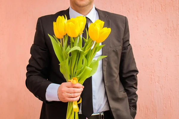 A man wearing business suit, holding bouquet of yellow tulips.