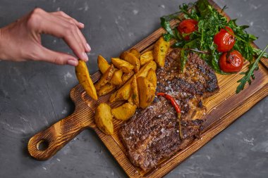 Tahta bir tahtada patates dilimli acı biberli biftek.